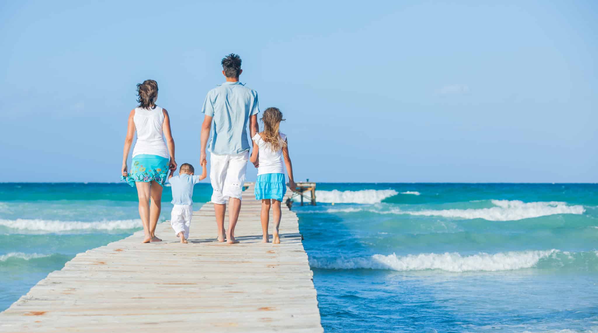 Family of four on wooden jetty by the ocean. Back view